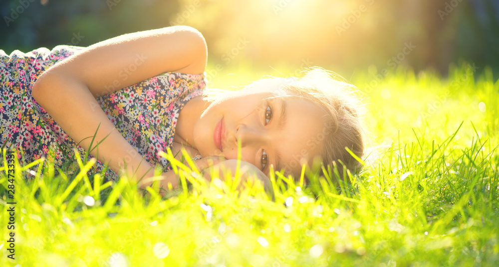 Portrait of a smiling little girl lying on green grass. Cute six years old child enjoying nature in summer park on a lawn Portrait of a smiling little girl lying on green grass. Cute six years old child enjoying nature in summer park on a lawn