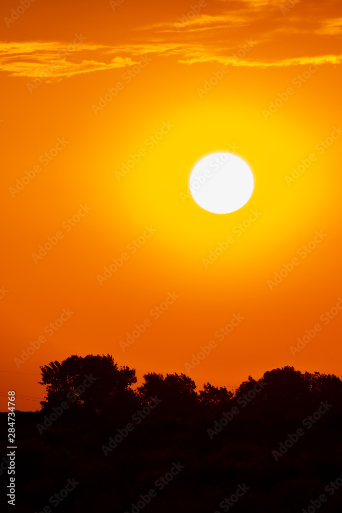 Bright sun in an orange sky with clouds at sunset