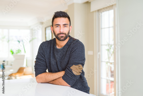 Handsome hispanic man wearing casual sweater at home skeptic and nervous, disapproving expression on face with crossed arms. Negative person.