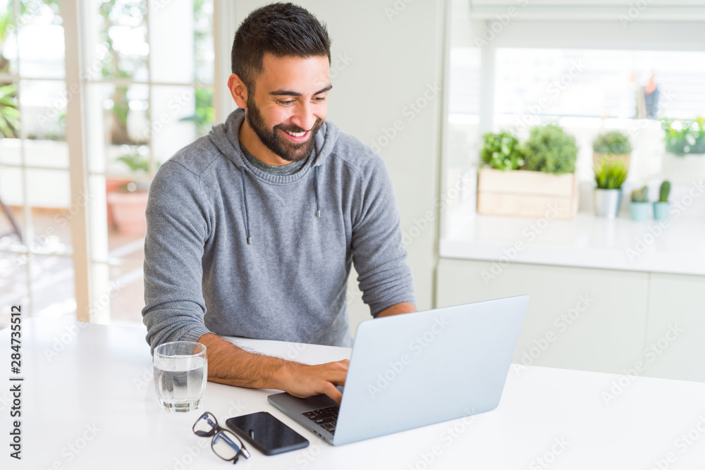 Handsome hispanic man working using computer laptop with a happy face standing and smiling with a confident smile showing teeth Handsome hispanic man working using computer laptop with a happy face standing and smiling with a confident smile showing teeth