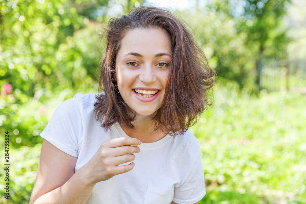 Happy girl smiling outdoor. Beautiful young brunete woman with brown hair resting on park or garden green background. European woman. Positive human emotion facial expression body language Happy girl smiling outdoor. Beautiful young brunete woman with brown hair resting on park or garden green background. European woman. Positive human emotion facial expression body language