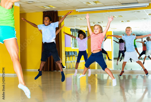 Group of tweens jumping with female coach during exercising in c