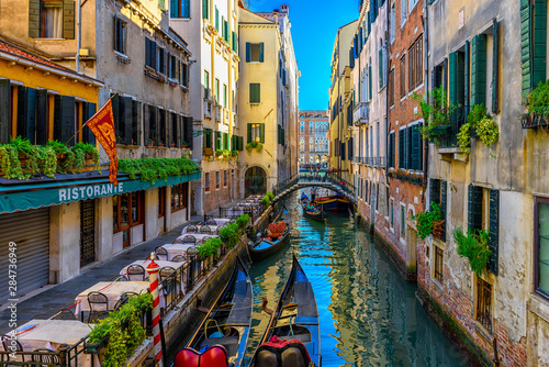 Fototapeta Narrow canal with gondola and tables of restaurant in Venice, Italy