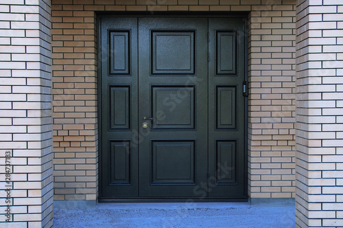 Black metal entrance door in a brick house. © Iuliia Alekseeva