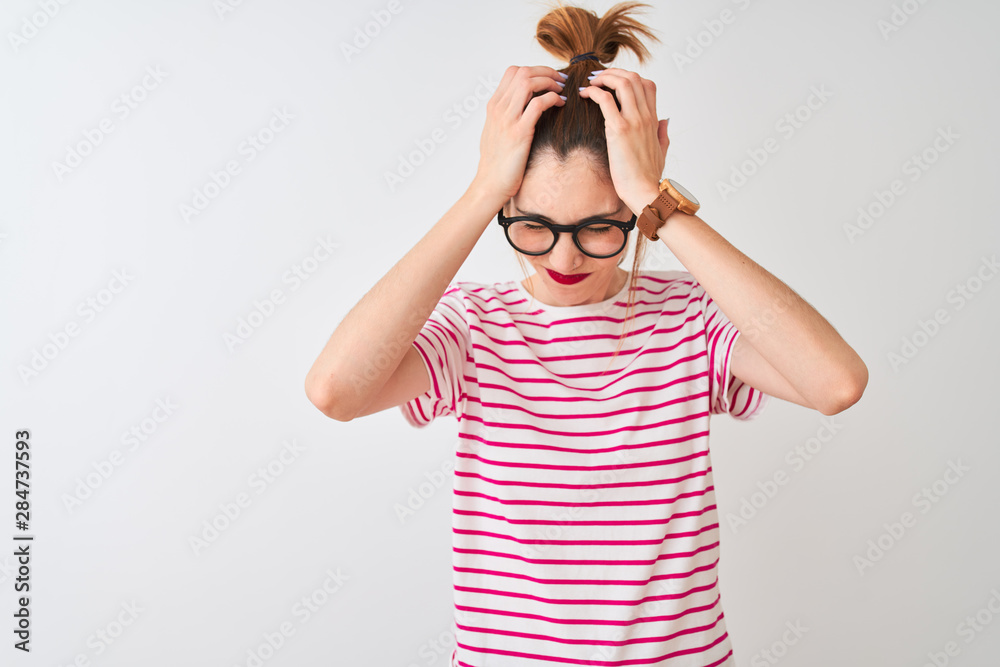 Redhead woman wearing glasses striped t-shirt and pigtail over isolated white background suffering from headache desperate and stressed because pain and migraine. Hands on head. Redhead woman wearing glasses striped t-shirt and pigtail over isolated white background suffering from headache desperate and stressed because pain and migraine. Hands on head.
