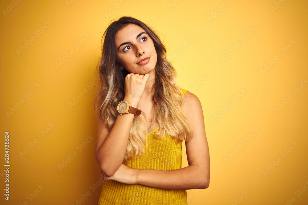 Young beautiful woman wearing t-shirt over yellow isolated background with hand on chin thinking about question, pensive expression. Smiling with thoughtful face. Doubt concept.
