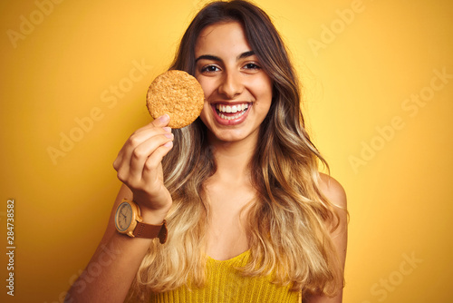 Young beautiful woman eating biscuit over grey isolated background with a happy face standing and smiling with a confident smile showing teeth