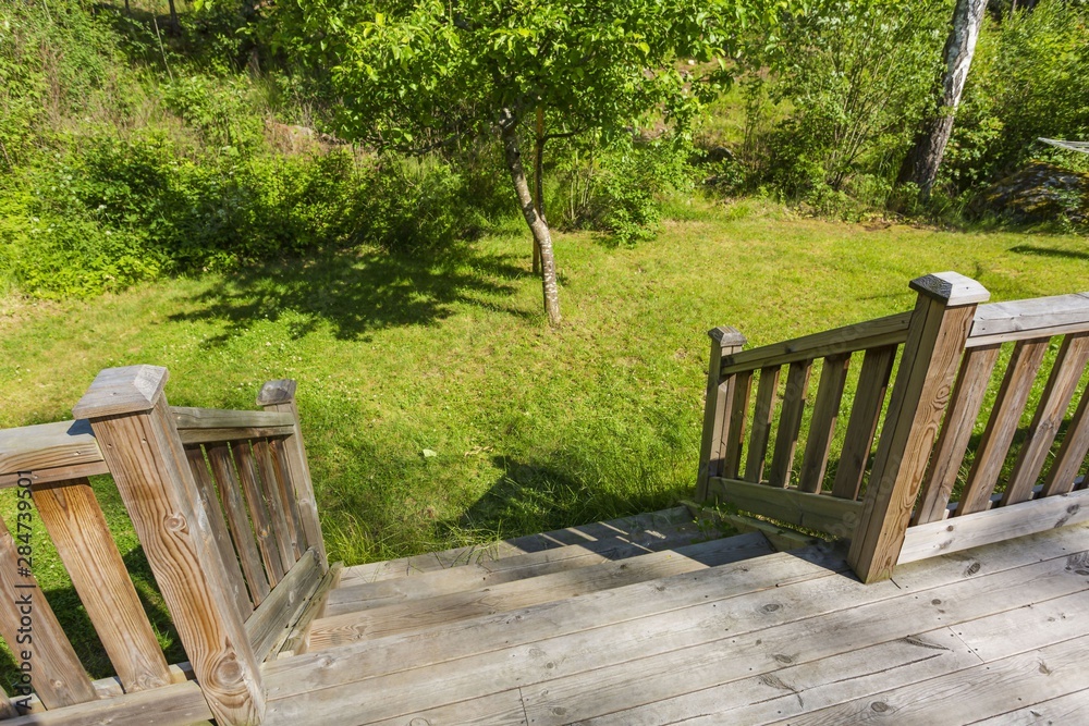 View of woode down stair from wooden terrace to back yard. Green trees and plants on background. Sweden. Europe. View of woode down stair from wooden terrace to back yard. Green trees and plants on background. Sweden. Europe.