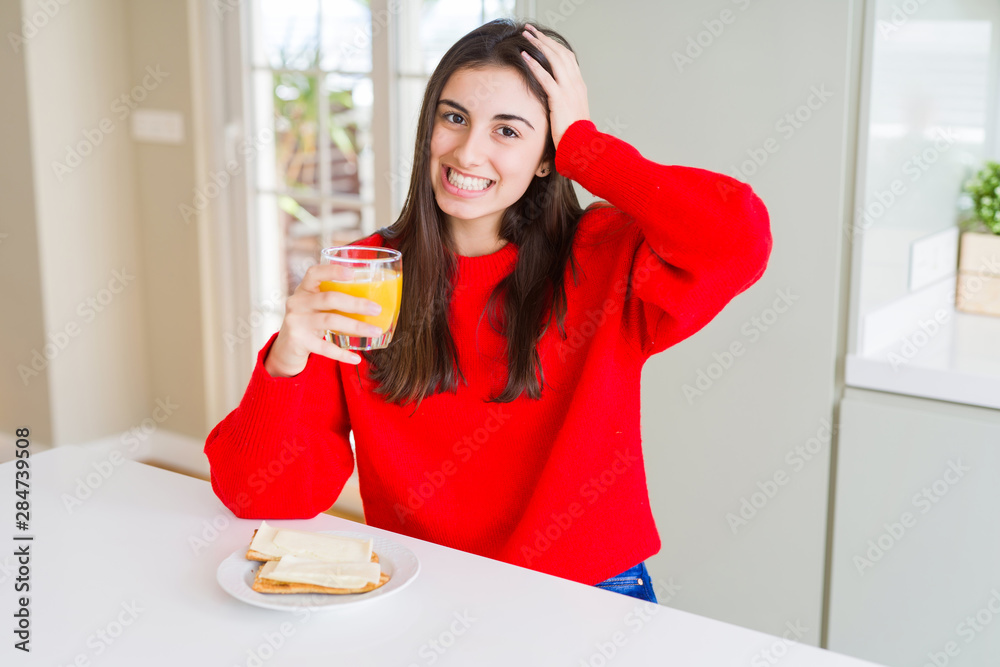 Beautiful young woman eating toasts and orange juice for snack or breakfast stressed with hand on head, shocked with shame and surprise face, angry and frustrated. Fear and upset for mistake.