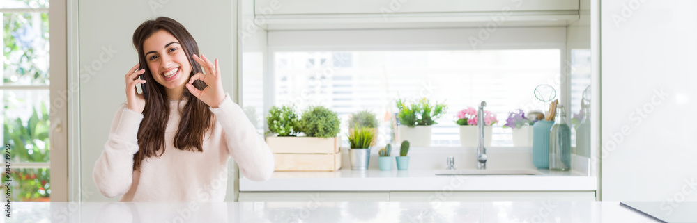 Wide angle picture of beautiful young woman having a conversation on smartphone doing ok sign with fingers, excellent symbol Wide angle picture of beautiful young woman having a conversation on smartphone doing ok sign with fingers, excellent symbol