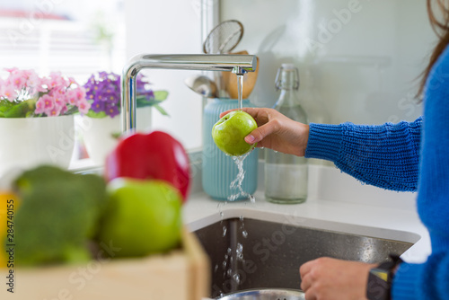 Young woman washing vegetables and fruit using water from sink