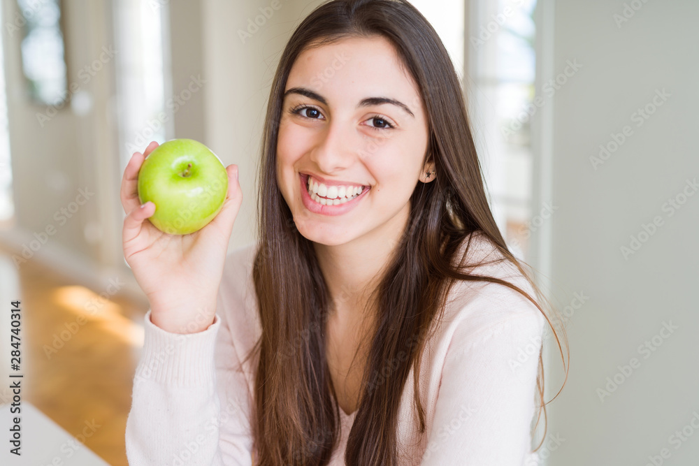 Beautiful young woman eating healthy green apple fruit with a happy face standing and smiling with a confident smile showing teeth Beautiful young woman eating healthy green apple fruit with a happy face standing and smiling with a confident smile showing teeth