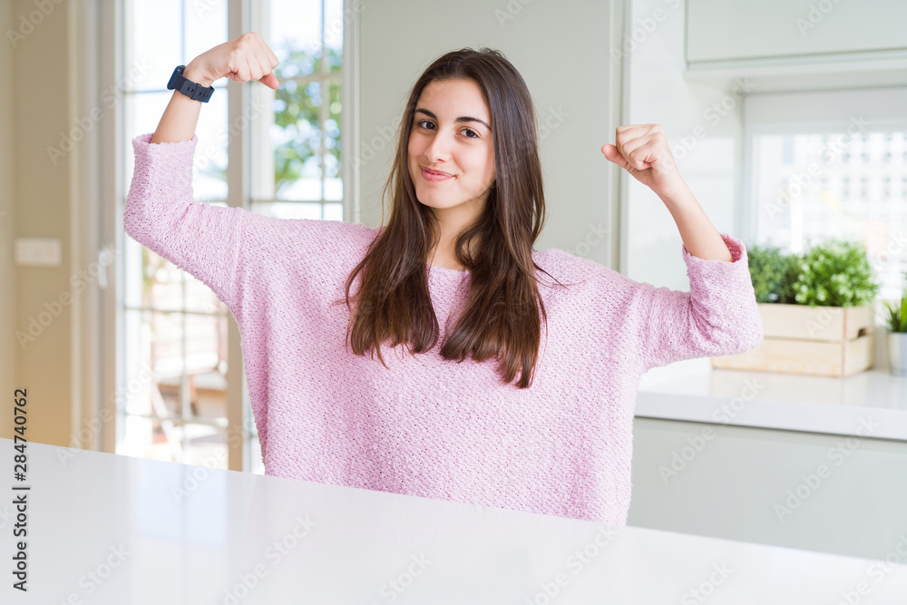 Beautiful young woman wearing pink sweater showing arms muscles smiling proud. Fitness concept. Beautiful young woman wearing pink sweater showing arms muscles smiling proud. Fitness concept.
