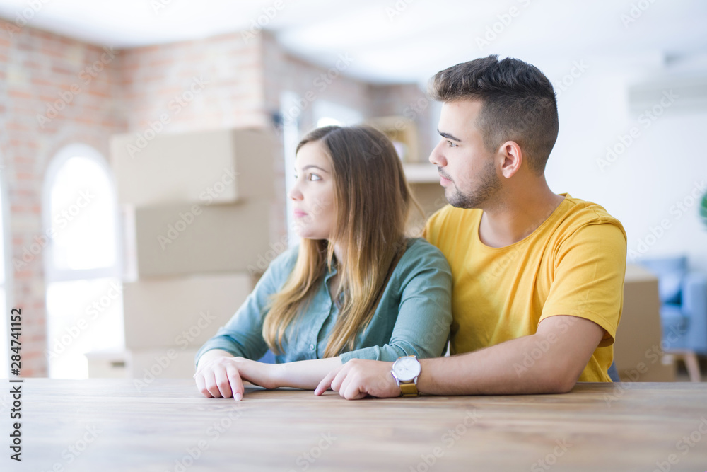 Young couple sitting on the table movinto to new home with carboard boxes behind them looking to side, relax profile pose with natural face with confident smile. Young couple sitting on the table movinto to new home with carboard boxes behind them looking to side, relax profile pose with natural face with confident smile.