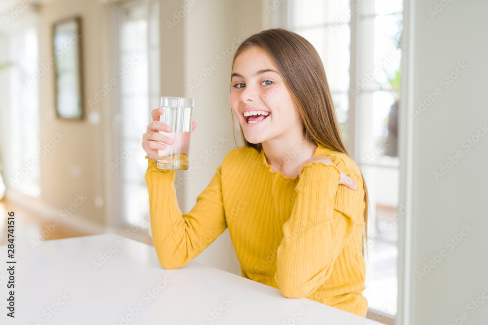 Beautiful young girl kid drinking a fresh glass of water with surprise face pointing finger to himself Beautiful young girl kid drinking a fresh glass of water with surprise face pointing finger to himself