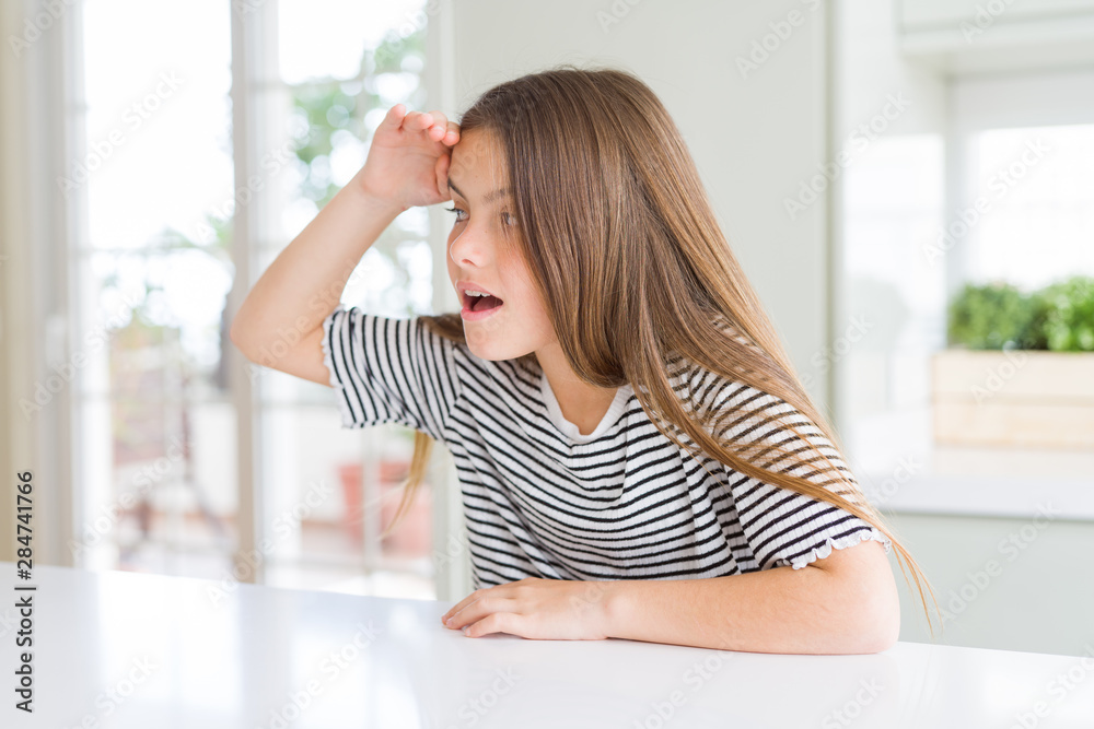 Beautiful young girl kid wearing stripes t-shirt very happy and smiling looking far away with hand over head. Searching concept.