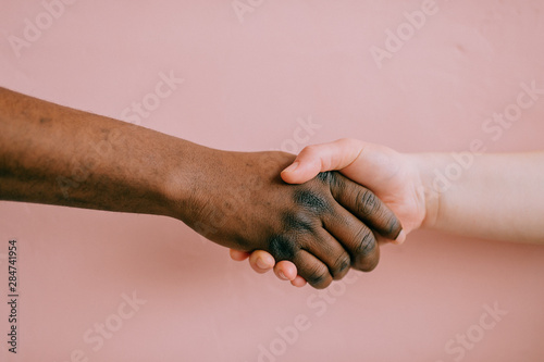 Handshake between african and caucasian male and female over pink background