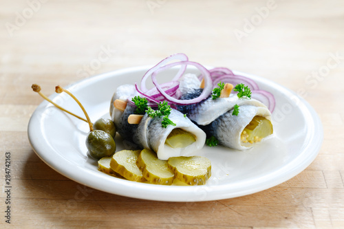 Photos rollmops or rolled pickled herring with red onions, gherkins and capers, a sour
