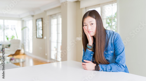 Young beautiful asian woman with long hair wearing denim jacket thinking looking tired and bored with depression problems with crossed arms.