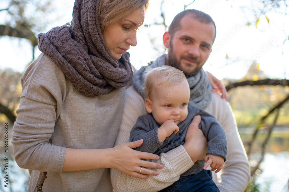 Fototapeta premium Happy family couple with their little child in autumn park in sunny day.