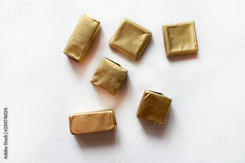Chocolate candies wrapped in golden foil isolated on white surface. Template for greeting card, poster or invitation. Sweets scattered on white smooth table. Backdrop or background