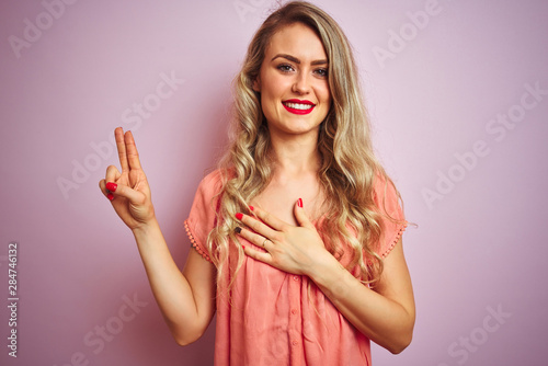 Young beautiful woman wearing t-shirt standing over pink isolated background smiling swearing with hand on chest and fingers up, making a loyalty promise oath