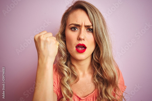 Young beautiful woman wearing t-shirt standing over pink isolated background annoyed and frustrated shouting with anger, crazy and yelling with raised hand, anger concept