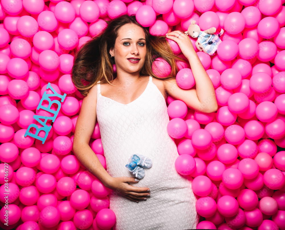 Fototapeta premium Young pregnant woman playing in a pink ball pool