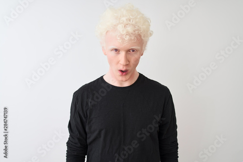 Young albino blond man wearing black t-shirt standing over isolated white background afraid and shocked with surprise expression, fear and excited face.