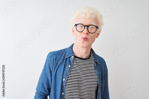 Young albino blond man wearing denim shirt and glasses over isolated white background looking at the camera blowing a kiss on air being lovely and sexy. Love expression.