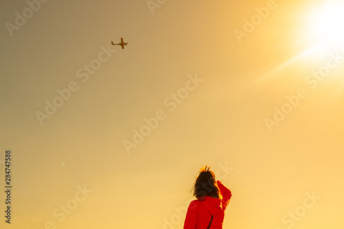 Woman watching a plane flying through the sky. Plane flying on sunset. Copy space for text.