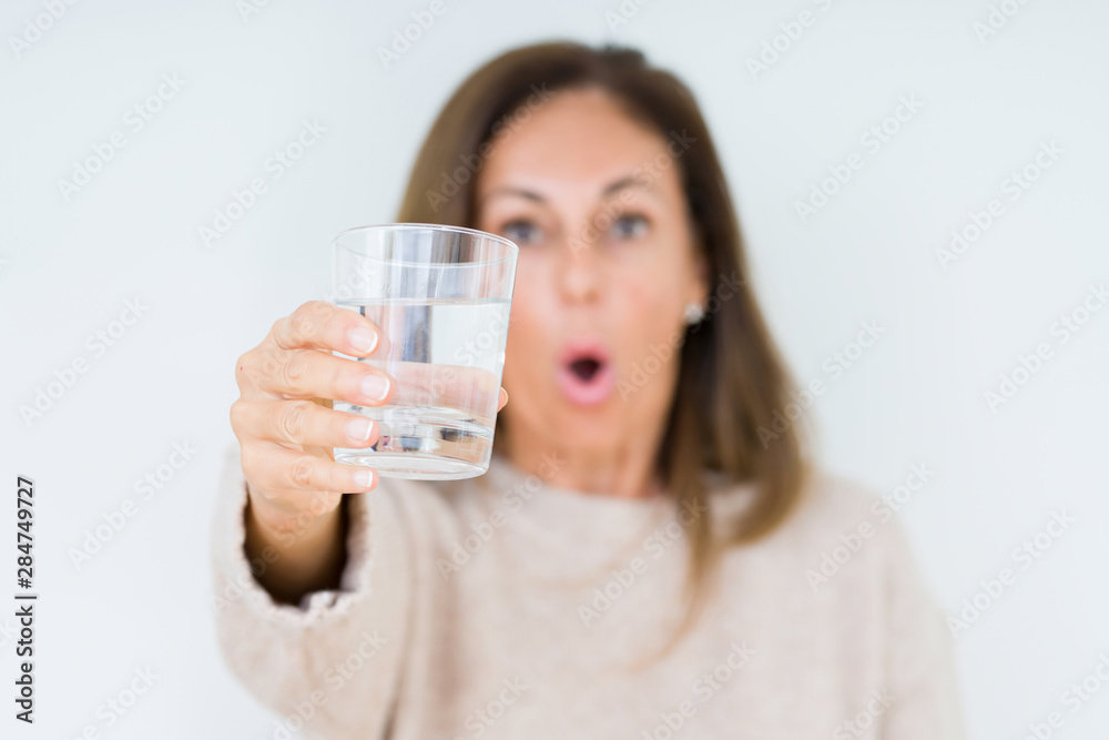 Middle age woman drinking glass of water isolated background scared in shock with a surprise face, afraid and excited with fear expression Middle age woman drinking glass of water isolated background scared in shock with a surprise face, afraid and excited with fear expression