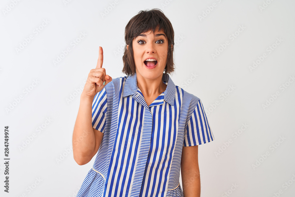 Young beautiful woman wearing blue striped shirt standing over isolated white background pointing finger up with successful idea. Exited and happy. Number one. Young beautiful woman wearing blue striped shirt standing over isolated white background pointing finger up with successful idea. Exited and happy. Number one.