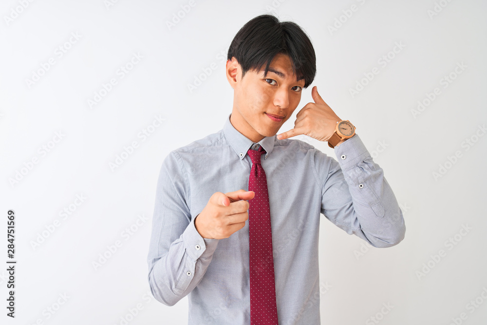 Chinese businessman wearing elegant tie standing over isolated white background smiling doing talking on the telephone gesture and pointing to you. Call me. Chinese businessman wearing elegant tie standing over isolated white background smiling doing talking on the telephone gesture and pointing to you. Call me.