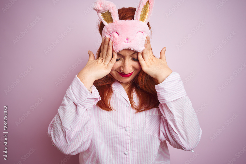 Young beautiful redhead woman wearing pajama over pink isolated background suffering from headache desperate and stressed because pain and migraine. Hands on head. Young beautiful redhead woman wearing pajama over pink isolated background suffering from headache desperate and stressed because pain and migraine. Hands on head.
