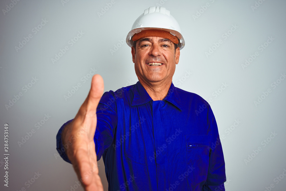 Handsome middle age worker man wearing uniform and helmet over isolated white background smiling friendly offering handshake as greeting and welcoming. Successful business.