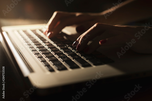 Closeup woman's hands typing on a laptop, having workplace at home, searching web, browsing information, with sunset light, dark shadows. Woman worker and business concept..