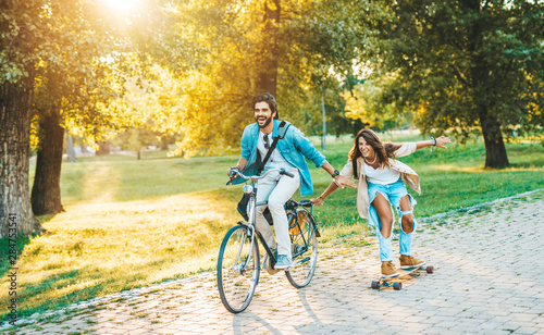 Beautiful young couple enjoying outdoors and riding bicycle in city skateboarding park