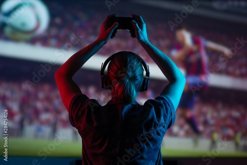 Canvastavla Soccer game, girl gamer playing a game in football headphones on a big screen, with bright light and a dark room