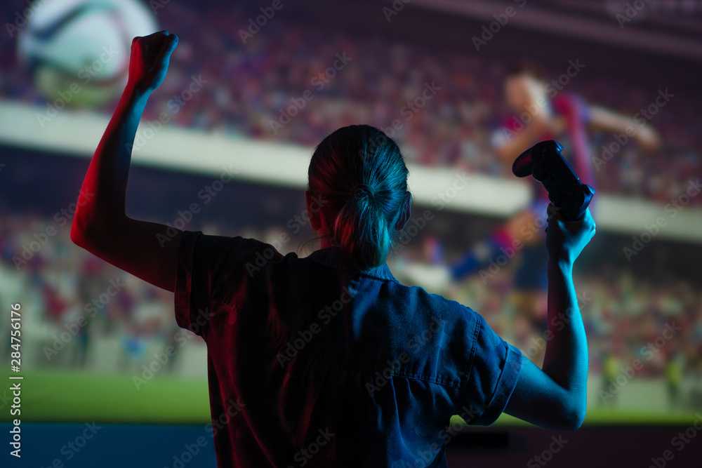 Soccer game, girl gamer playing a game in football headphones on a big screen, with bright light and a dark room. Gameplay, streaming, e-sports.