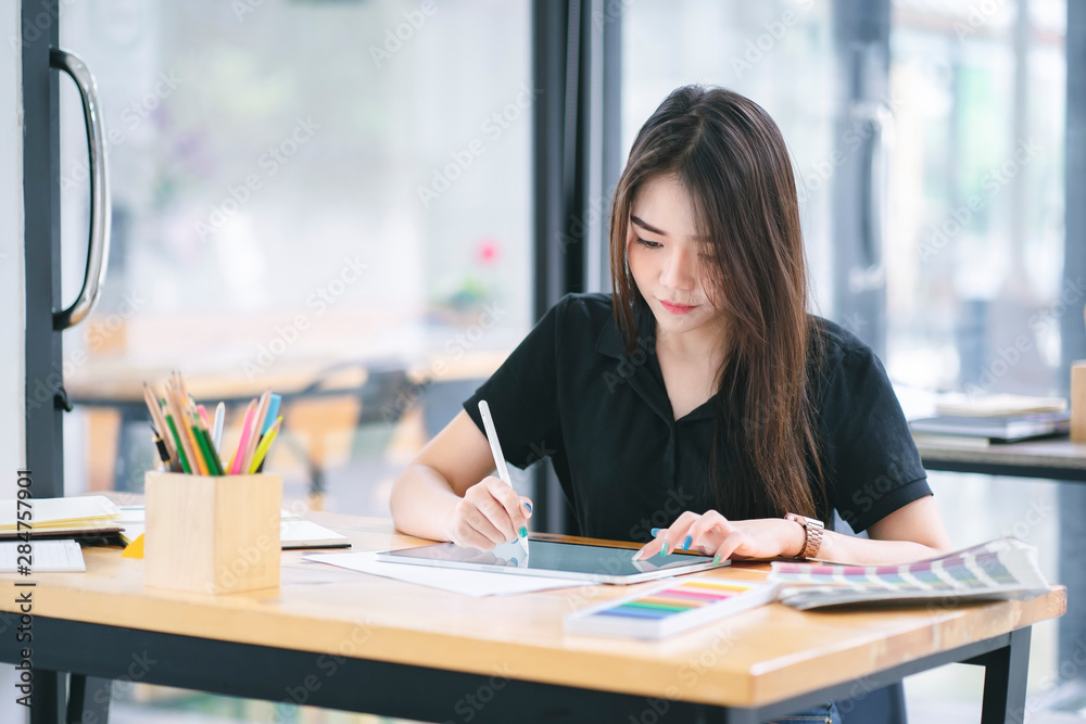 Young Asian graphic designer working on computor and graphics tablet in her working space