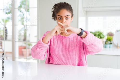 Beautiful african american woman with afro hair wearing casual pink sweater Rejection expression crossing fingers doing negative sign