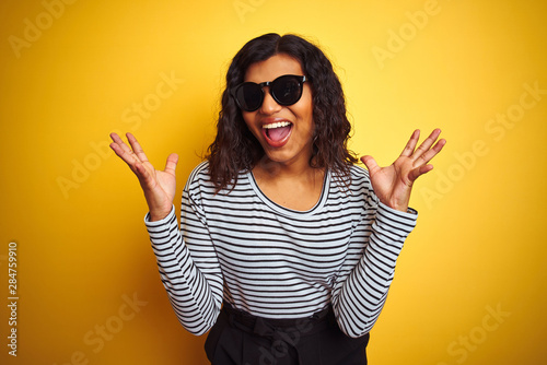 Transsexual transgender woman wearing sunglasses over isolated yellow background celebrating crazy and amazed for success with arms raised and open eyes screaming excited. Winner concept