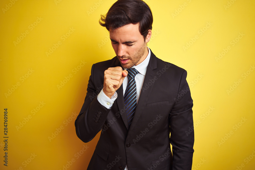 Young handsome businessman wearing suit and tie standing over isolated yellow background feeling unwell and coughing as symptom for cold or bronchitis. Healthcare concept. Young handsome businessman wearing suit and tie standing over isolated yellow background feeling unwell and coughing as symptom for cold or bronchitis. Healthcare concept.