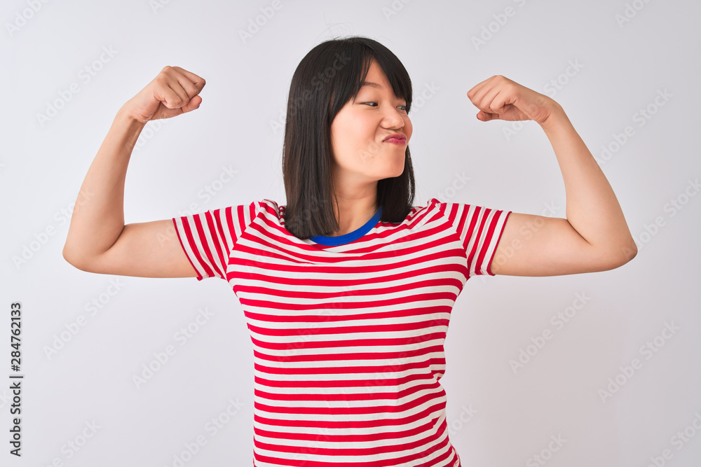 Young beautiful chinese woman wearing red striped t-shirt over isolated white background showing arms muscles smiling proud. Fitness concept.