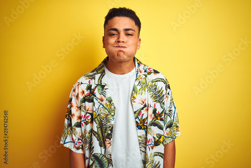 Wallpaper Mural Young brazilian man on vacation wearing summer floral shirt over isolated yellow background puffing cheeks with funny face. Mouth inflated with air, crazy expression. Torontodigital.ca