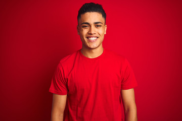 Young brazilian man wearing t-shirt standing over isolated red background with a happy and cool smile on face. Lucky person.