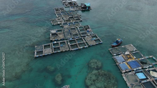 At one exotic island in Vietnam, flying over fishing boats and tranquil floating houses with sea corals underneath crystal clear blue water. Phan Thiet, Vietnam. Pan shot. photo