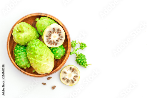 Fresh raw and ripe Morinda citrifolia or Noni fruit and sliced with seeds in wooden bowl isolated on white background.