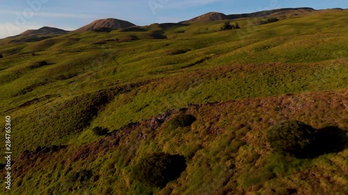 aerial of green grassy fields on the upper Kohala road near Waimea. hills and cinder cones in the distance, flying. low over pasture land. photo